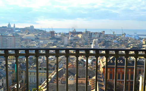 Genoa cityscape view from a balcony, featuring historic buildings and the harbor in the distance.
