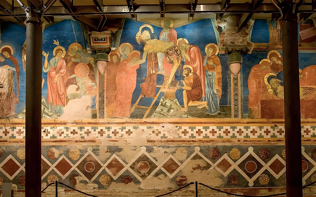 Tour group viewing frescoes in Siena Cathedral Crypt, Italy, with vibrant religious scenes.