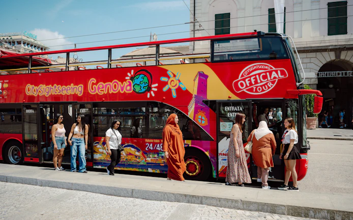 Tourists boarding Genova city sightseeing bus with guide in front of historic building.