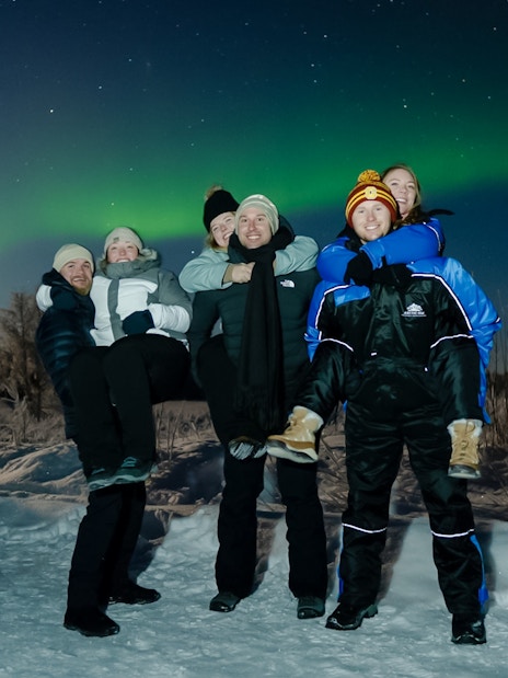 Small group enjoying Northern Lights in snowy Rovaniemi landscape.