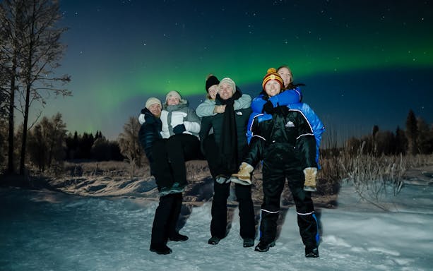Small group enjoying Northern Lights in snowy Rovaniemi landscape.
