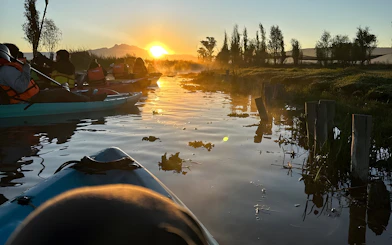 Kayaking at sunrise in Xochimilco canals with distant mountains.
