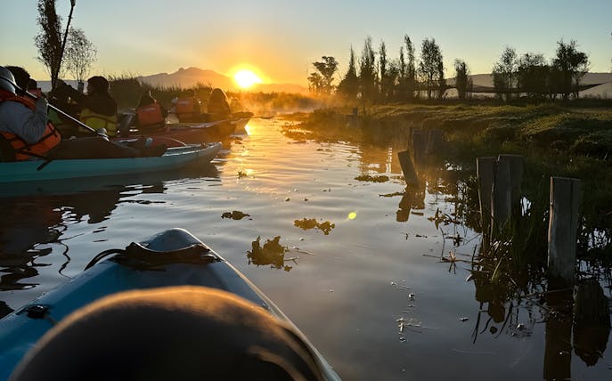 Kayaking at sunrise in Xochimilco canals with distant mountains.