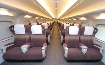 Shinkansen train interior with rows of comfortable seats and overhead lighting.