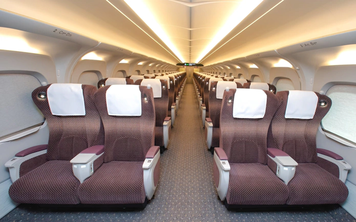 Shinkansen train interior with rows of comfortable seats and overhead lighting.