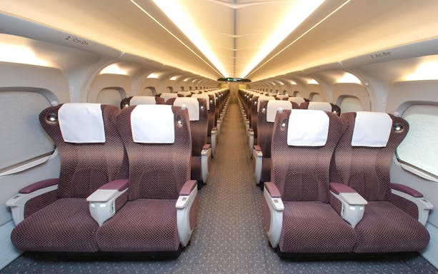 Shinkansen train interior with rows of comfortable seats and overhead lighting.