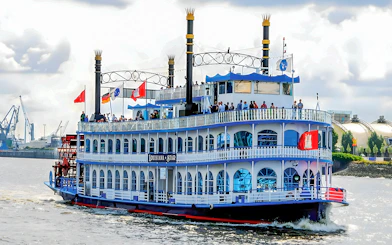 Paddle steamer on Hamburg Harbor cruise with passengers on deck, cityscape in background.
