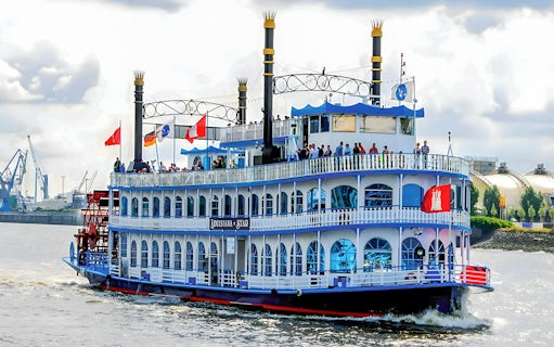 Paddle steamer on Hamburg Harbor cruise with passengers on deck, cityscape in background.