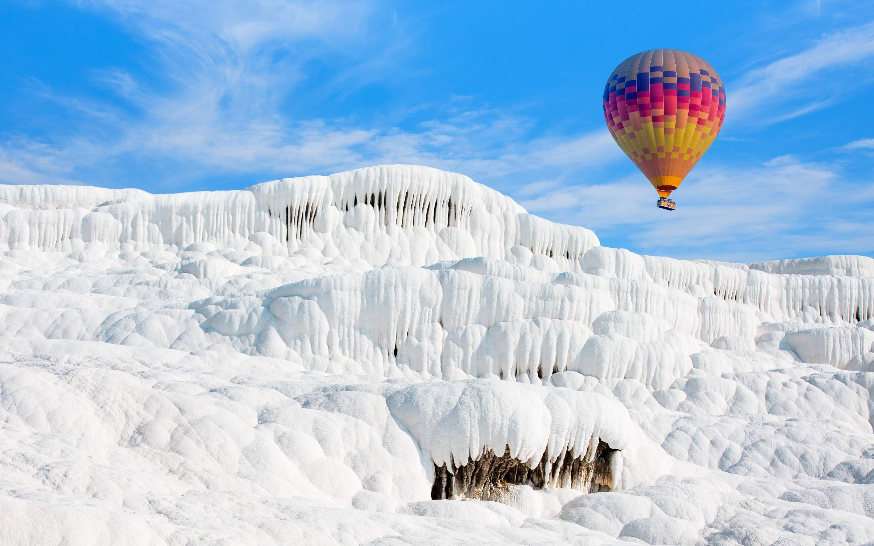 Hot air balloon over white travertine terraces in Pamukkale, Turkey.