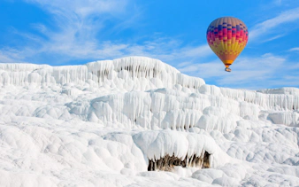 Hot air balloon over white travertine terraces in Pamukkale, Turkey.