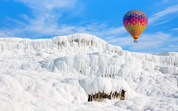Hot air balloon over white travertine terraces in Pamukkale, Turkey.