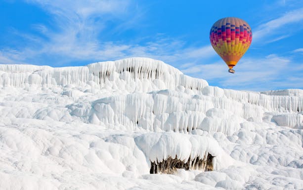 Hot air balloon over white travertine terraces in Pamukkale, Turkey.
