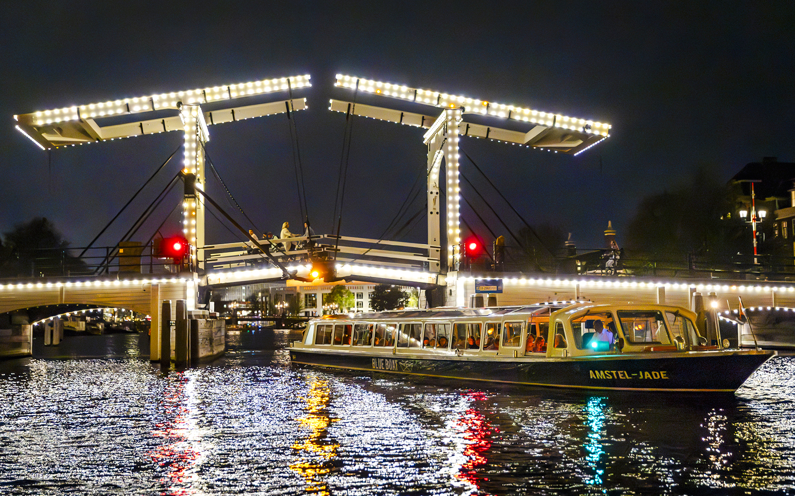 Evening cruise boat passing under illuminated bridge in Amsterdam.