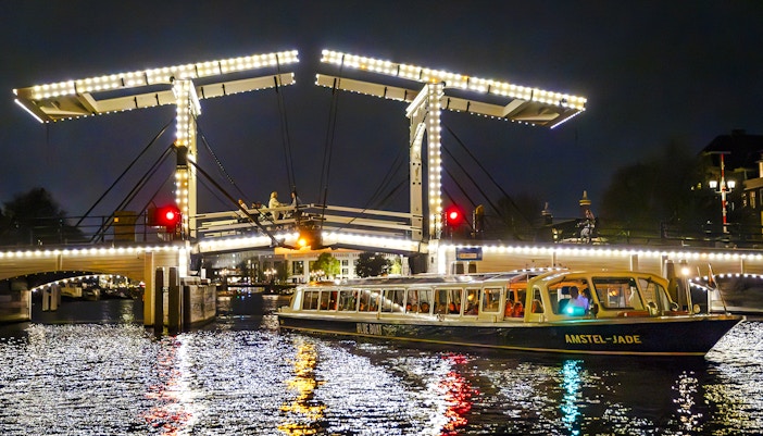 Evening cruise boat passing under illuminated bridge in Amsterdam.