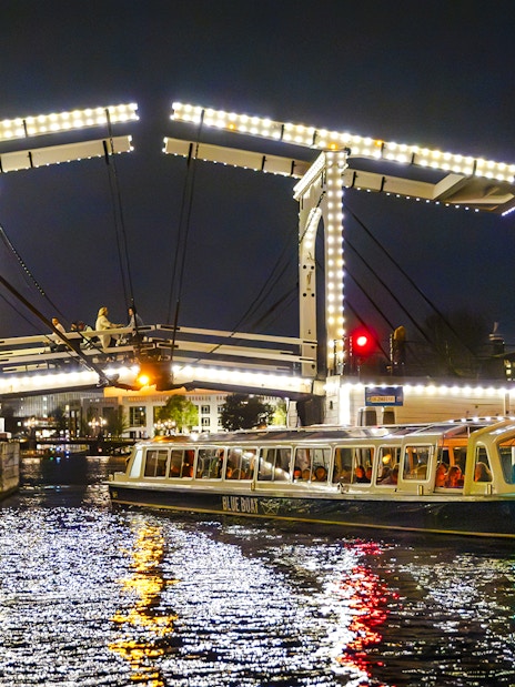 Evening cruise boat passing under illuminated bridge in Amsterdam.