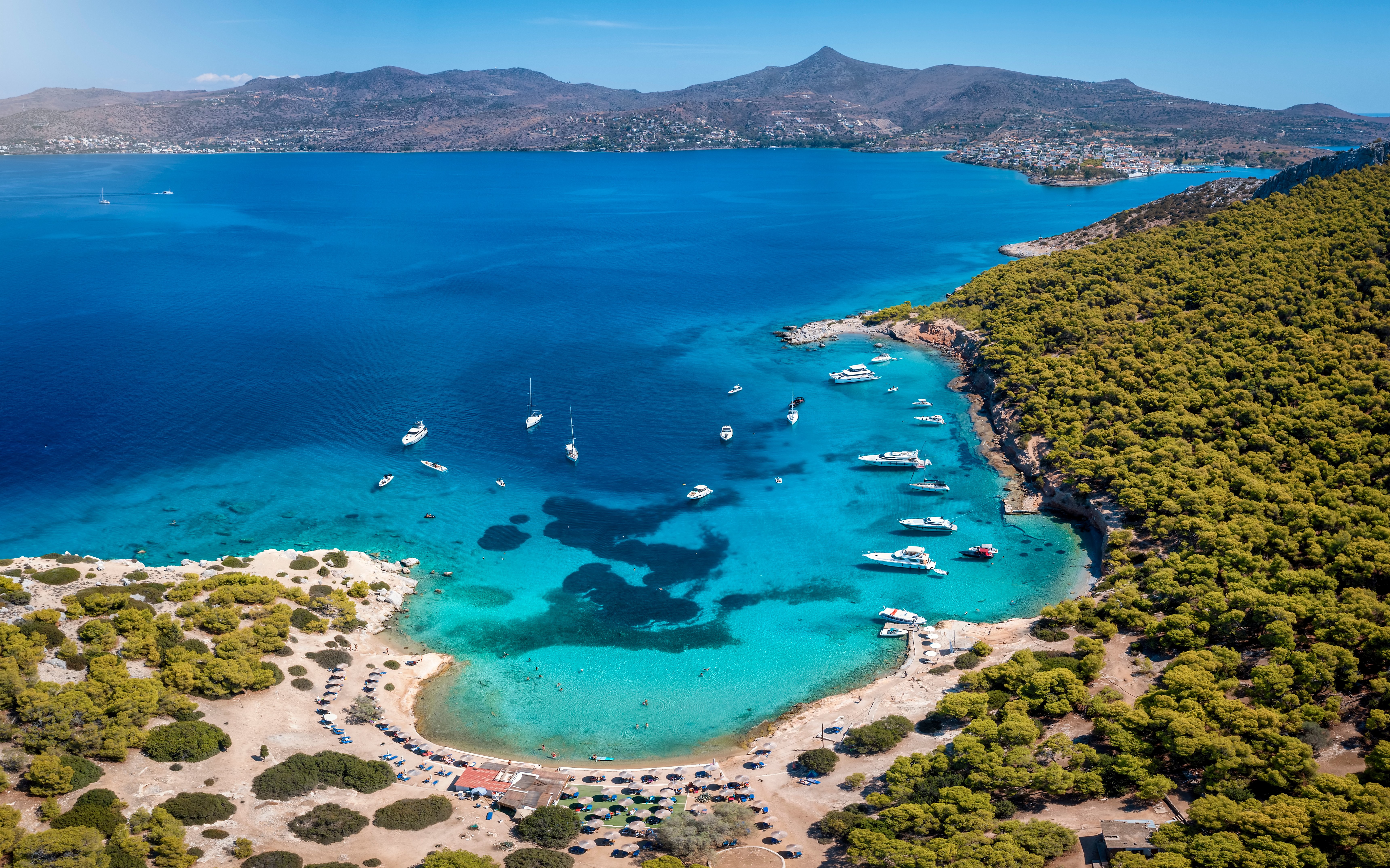 Aerial view of Moni island beach with boats in turquoise waters near Perdika, Aegina, Saronic Gulf, Greece.