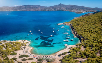 Aerial view of Moni island beach with boats in turquoise waters near Perdika, Aegina, Saronic Gulf, Greece.