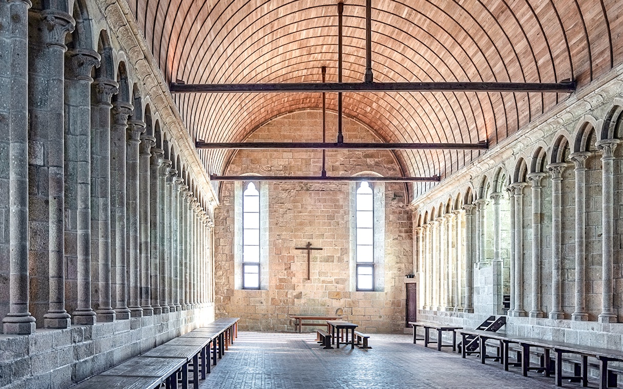 Mont-Saint-Michel Abbey interior with stone columns and wooden ceiling.