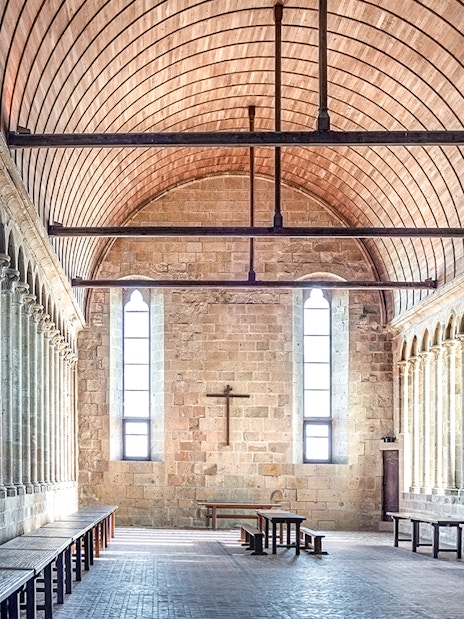 Mont-Saint-Michel Abbey interior with stone columns and wooden ceiling.