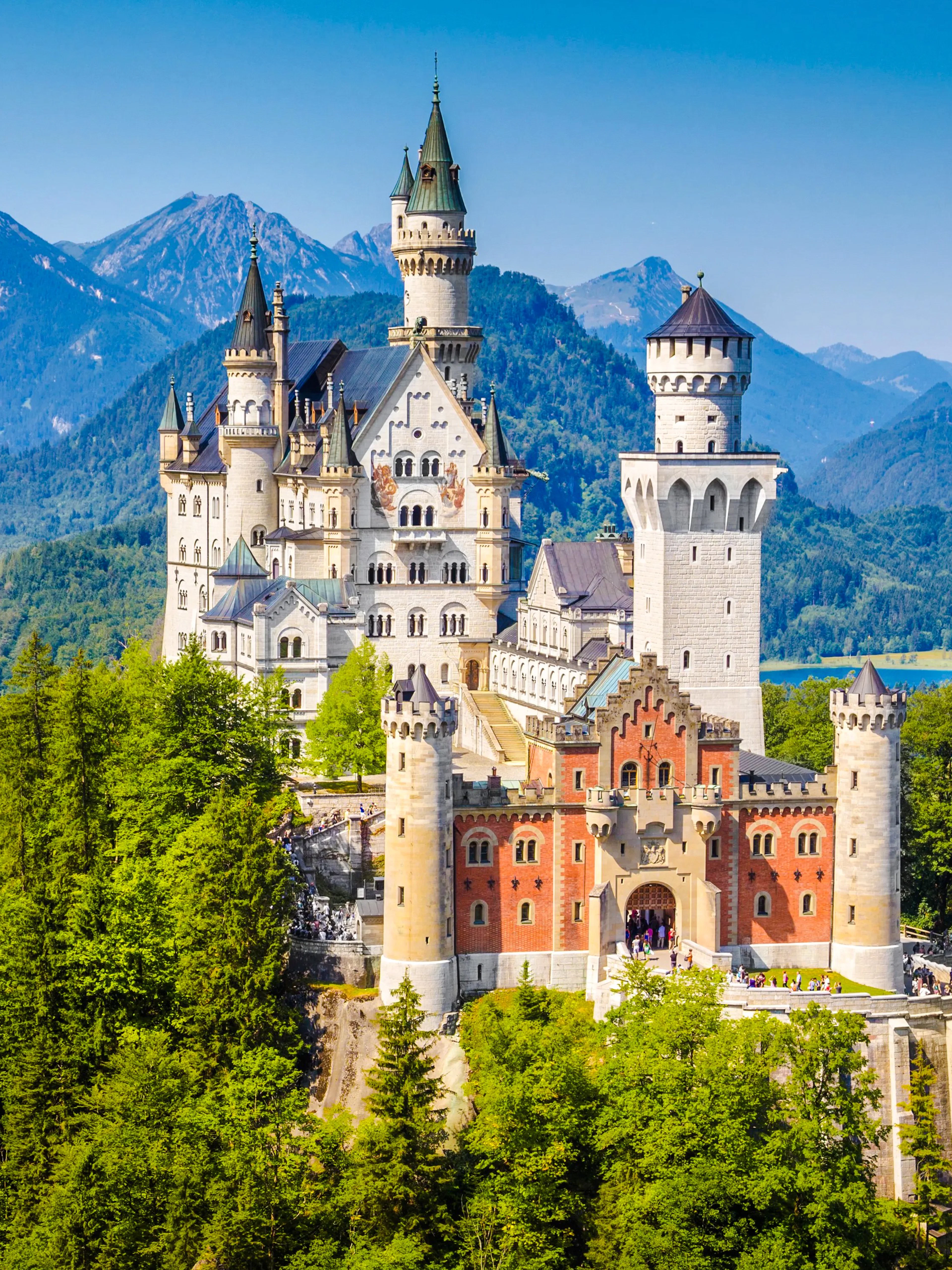 Neuschwanstein Castle exterior with forest and mountains in Bavaria, Germany.