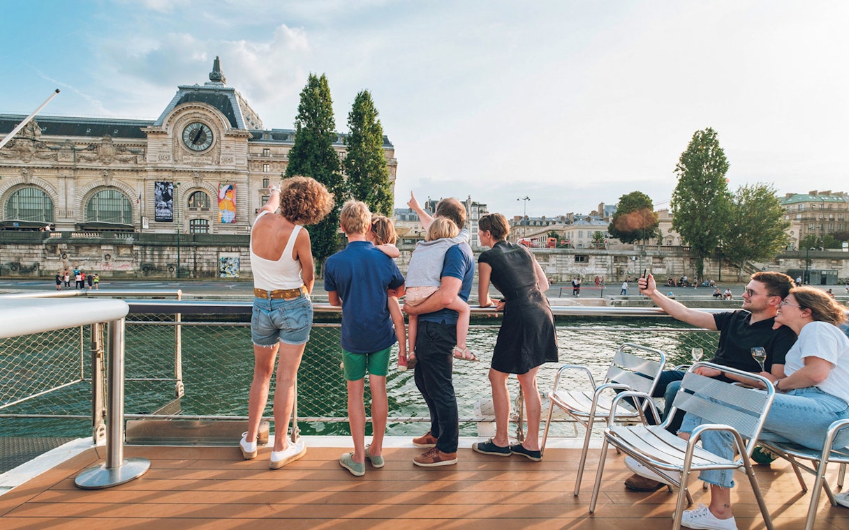 Family enjoying a Seine River cruise with a view of the Musée d'Orsay in Paris.