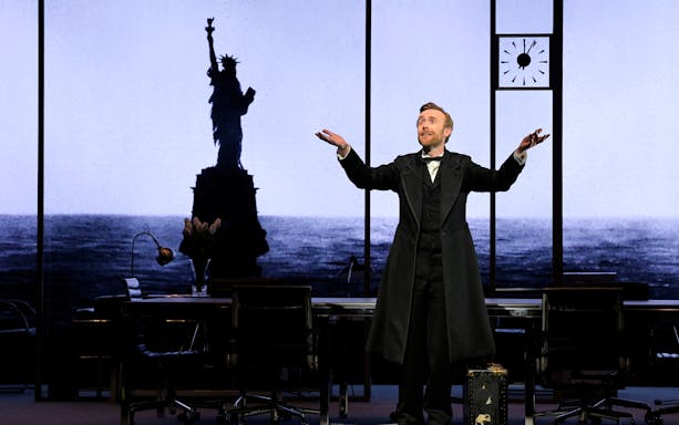 Actor on stage during "The Lehman Trilogy" with Statue of Liberty backdrop.