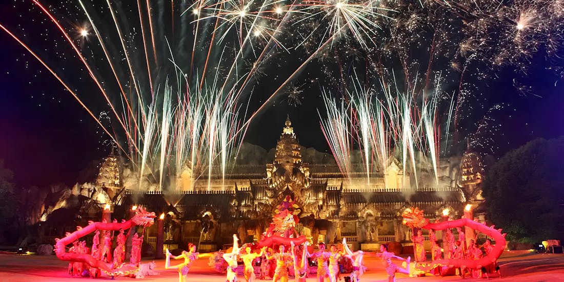pectacular night scene at Phuket Fantasea featuring a dazzling fireworks display with performers in traditional Thai costumes engaged in an elaborate dance in front of an ornate temple structure