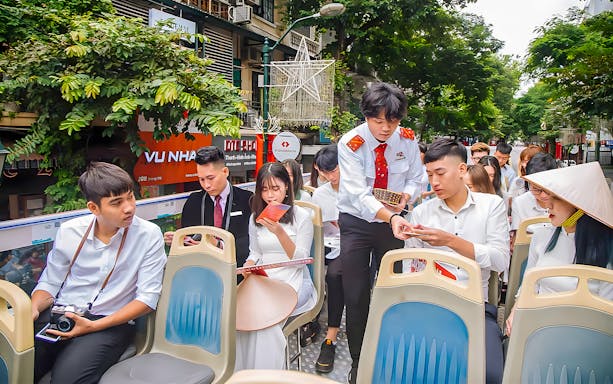 Passengers on Haanoi city hop-on hop-off tour bus reviewing brochures.