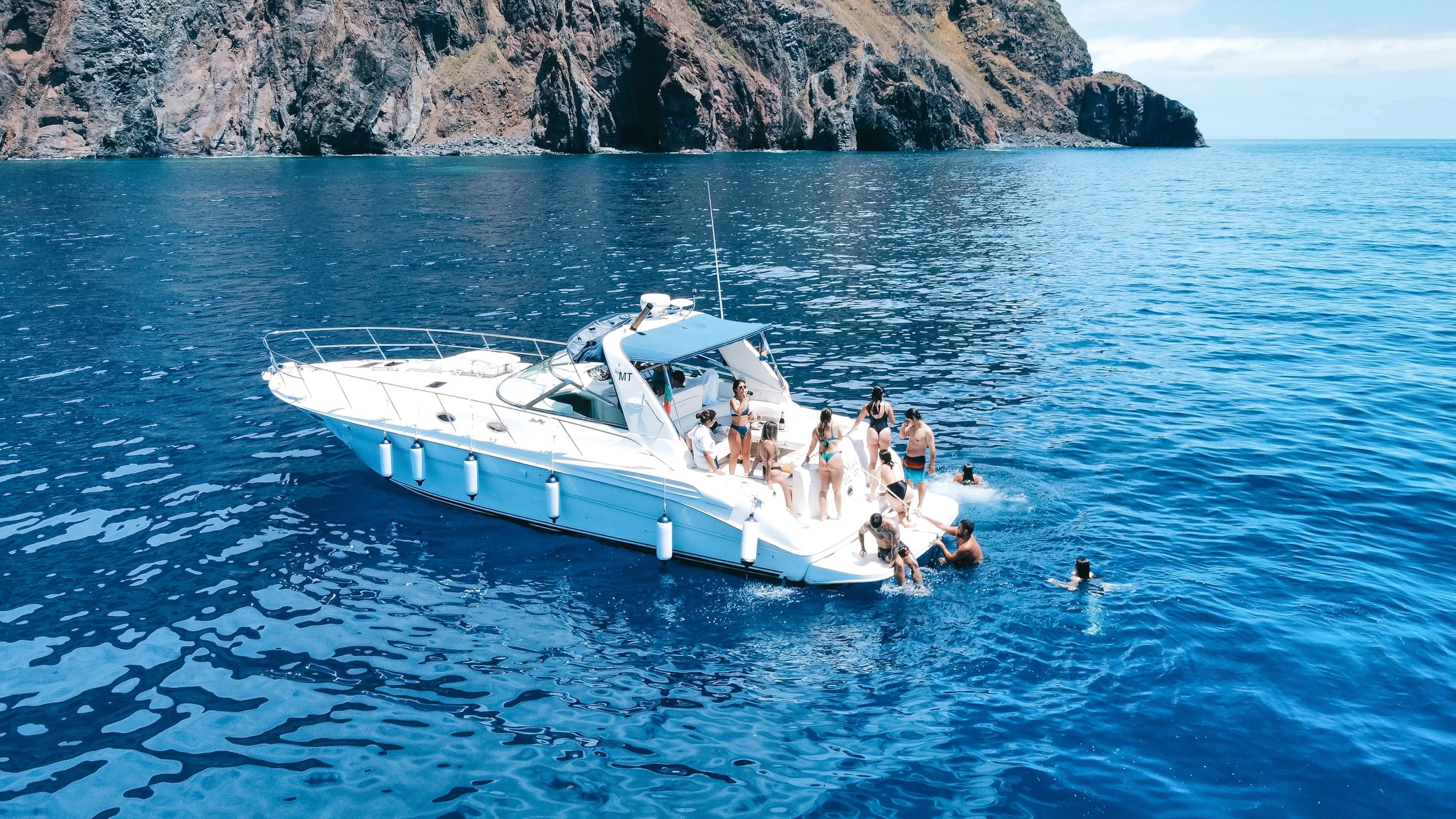 Boat tour near Calheta with people swimming in the ocean, rocky cliffs in the background.
