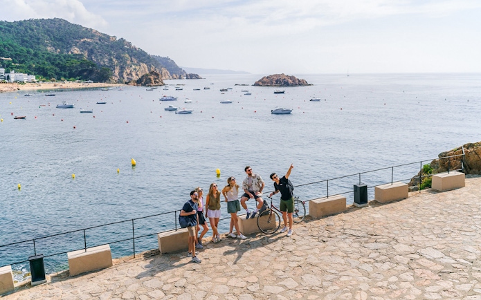 Tourists enjoying a scenic view of the Costa Brava coastline with boats in the water.
