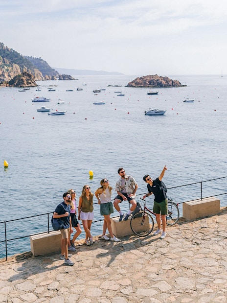 Tourists enjoying a scenic view of the Costa Brava coastline with boats in the water.