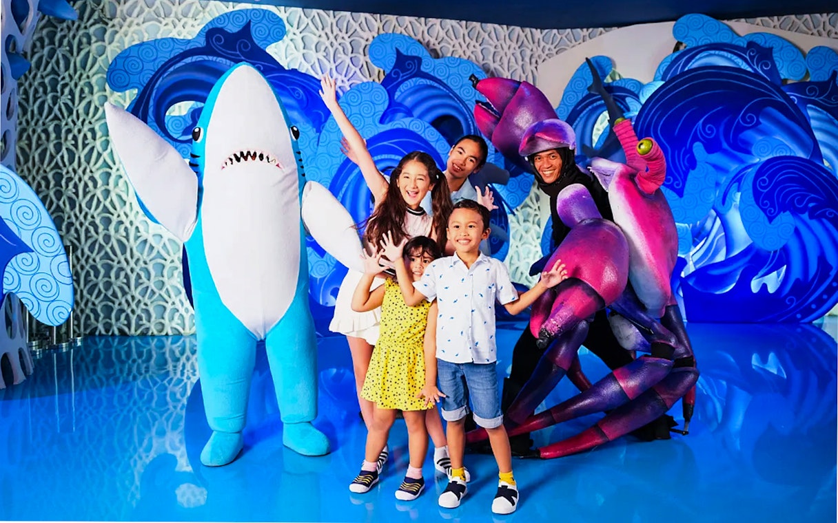 Tourists posing with shark and crab mascots at Jakarta Aquarium Safari.