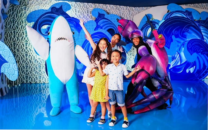 Tourists posing with shark and crab mascots at Jakarta Aquarium Safari.