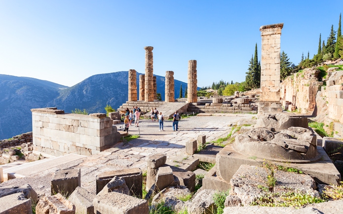 Visitors exploring the ancient ruins of the Temple of Apollo in Greece.