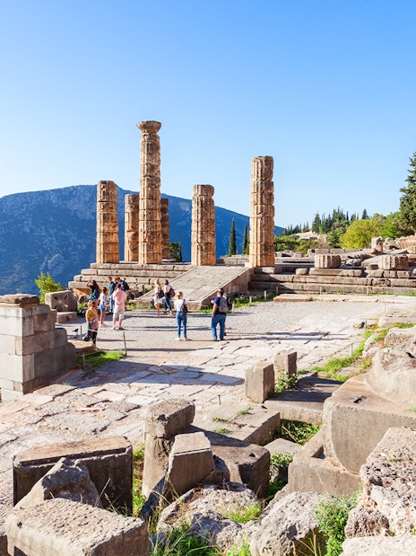 Visitors exploring the ancient ruins of the Temple of Apollo in Greece.