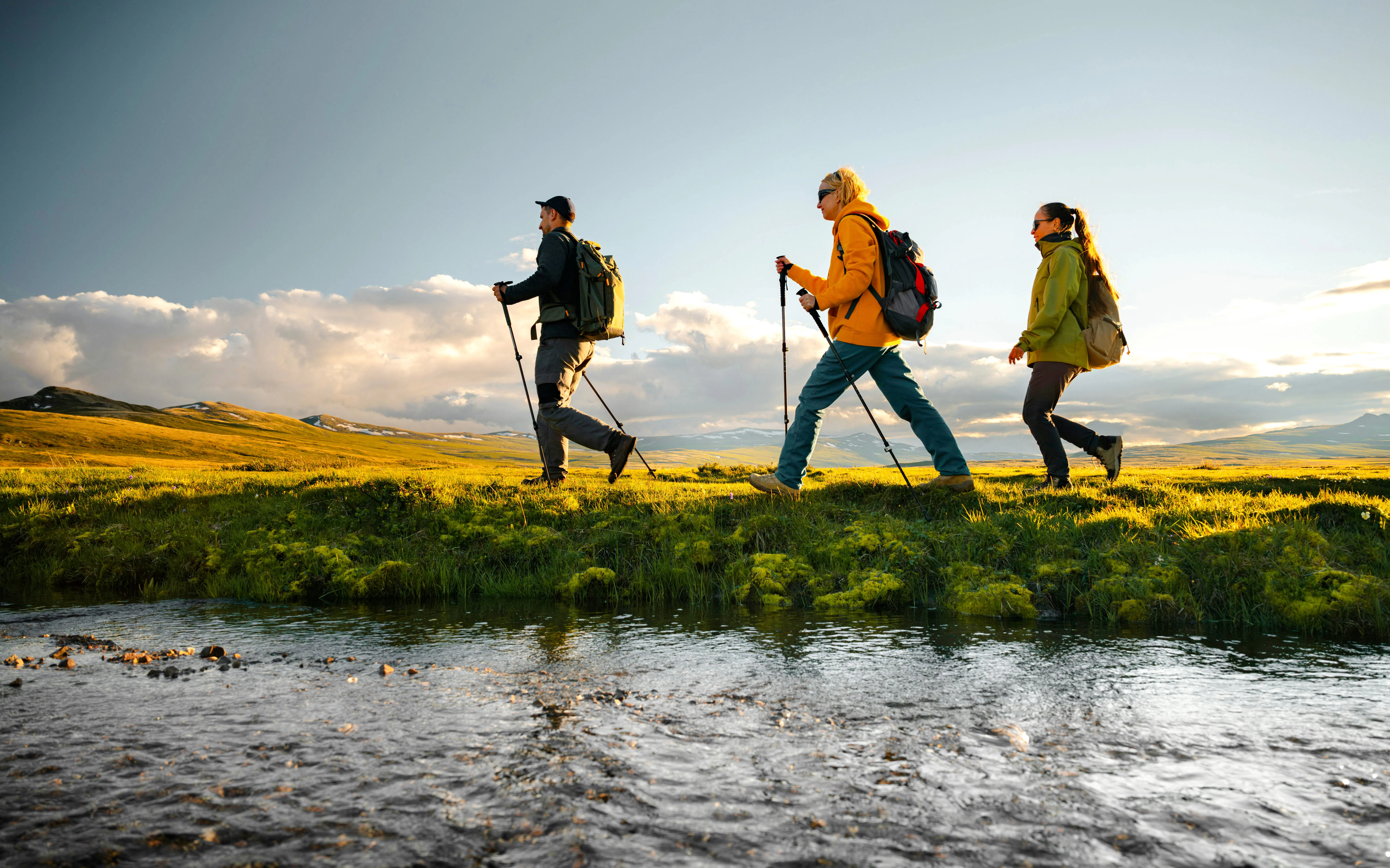 Hikers group with trekking poles walk along a stream on a mountain plateau at sunset, low angle view in scottish highlands