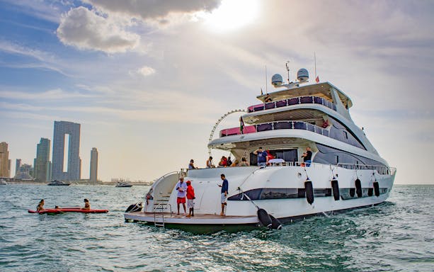 Super-yacht cruise in Dubai Marina with people enjoying the deck, city skyline in background.