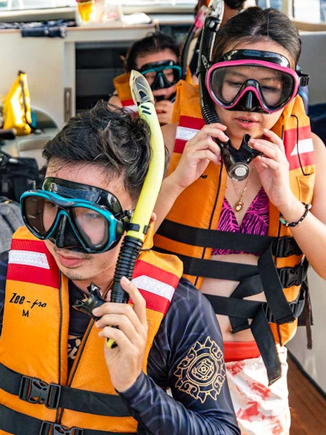 Tourists preparing for snorkeling at Nusa Penida, Bali, wearing life jackets and snorkel gear on a boat.