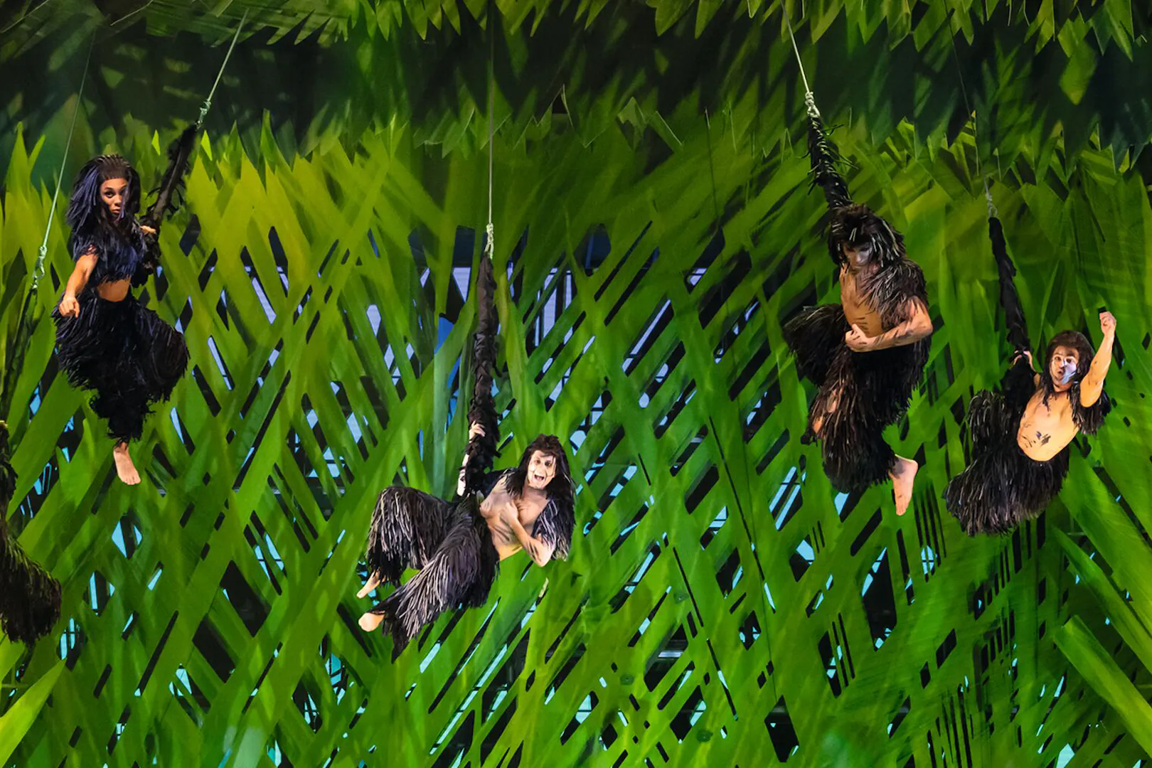 Performers in jungle costumes swinging on vines in Disney's Tarzan show.