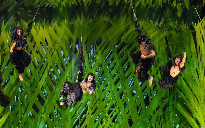 Performers in jungle costumes swinging on vines in Disney's Tarzan show.