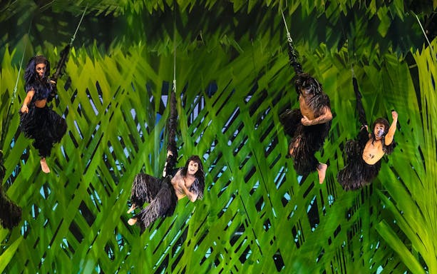 Performers in jungle costumes swinging on vines in Disney's Tarzan show.