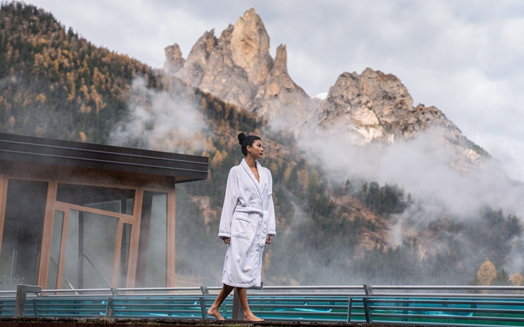 Person in a robe at QC Terme Dolomiti spa with mountain view in background.