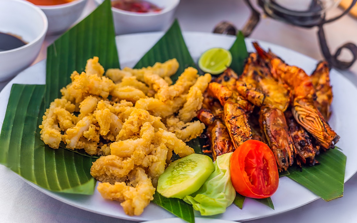 Grilled prawns and fried calamari on banana leaves, Jimbaran Bali seafood dinner.