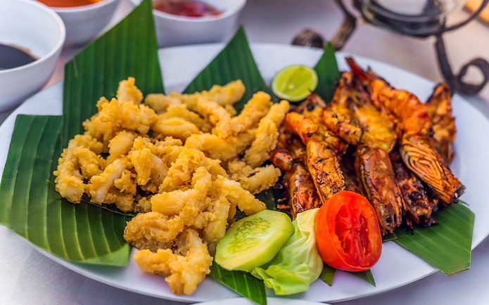 Grilled prawns and fried calamari on banana leaves, Jimbaran Bali seafood dinner.