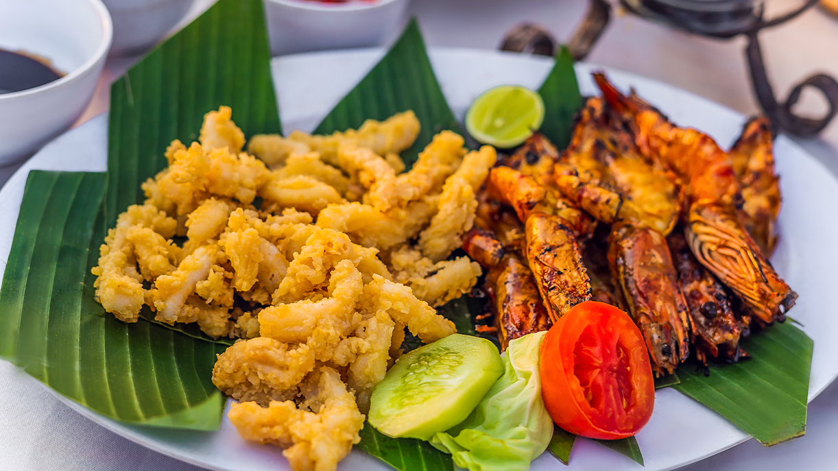 Grilled prawns and fried calamari on banana leaves, Jimbaran Bali seafood dinner.
