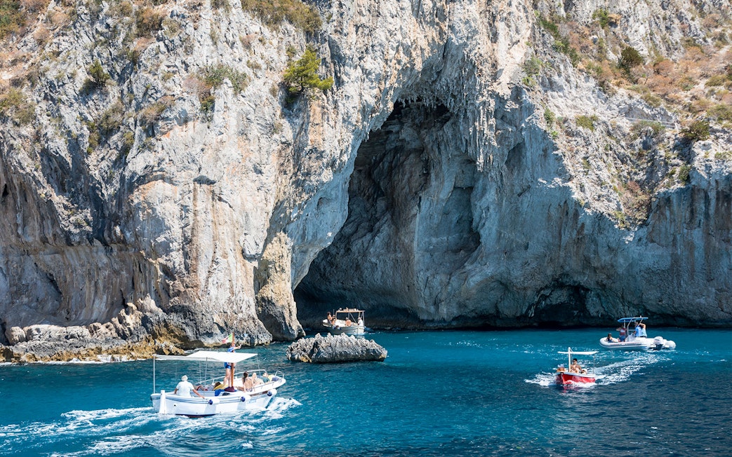 Boats navigating near a rocky cave on the coast of Capri, Italy.