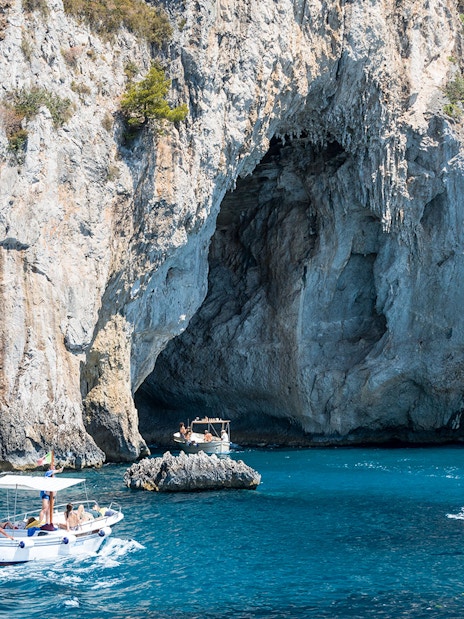 Boats navigating near a rocky cave on the coast of Capri, Italy.