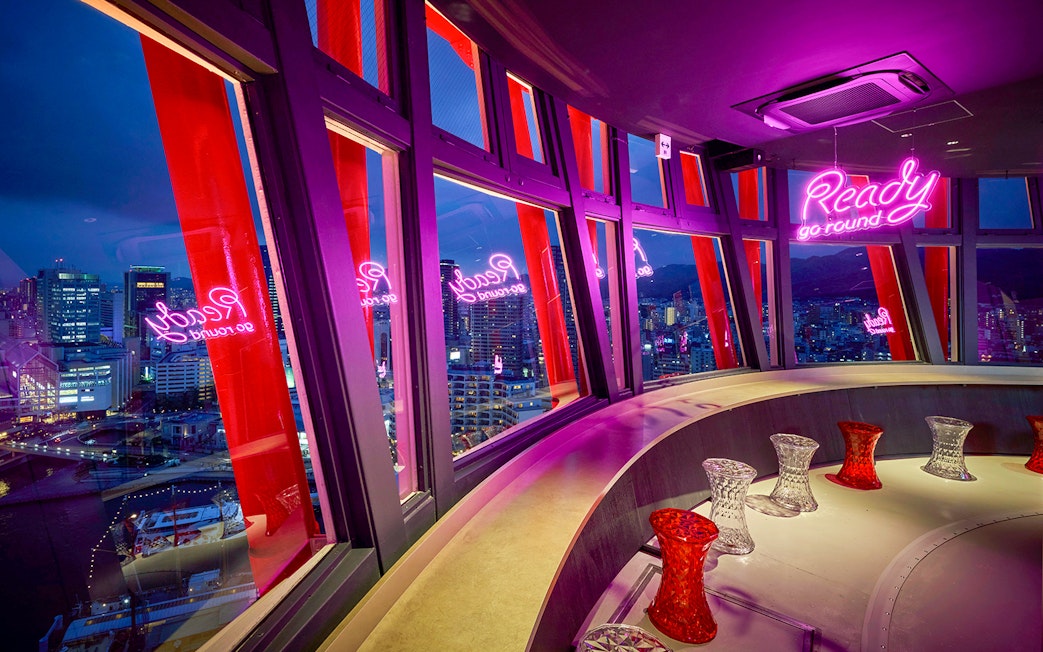 Kobe Port Tower interior view with cityscape and neon sign at night.