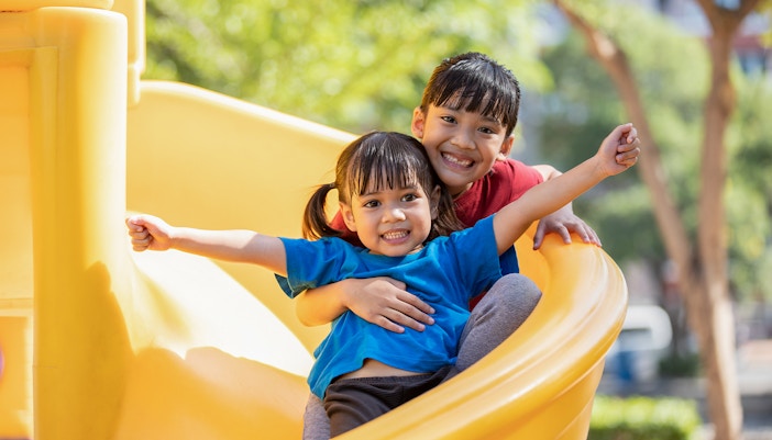 Children playing in a garden play area with colorful equipment in a city park.