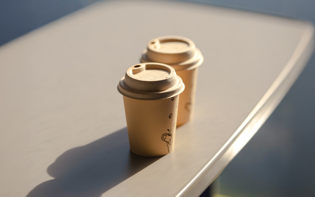 Two paper coffee cups with lids on a table.